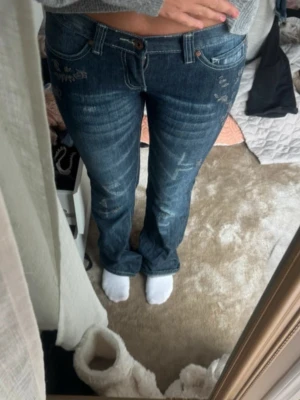 Blå bootcut jeans med broderi lågmidjade - LÄGG BUD!!!💕26/32 Säljer ett par mörkblå jeans med bootcut passform och snygga slitningar. Jeansen har broderade detaljer vid fickorna och klassisk femficksdesign. Materialet är jeans och de har låg midja. Perfekta för dig som gillar en avslappnad men ändå trendig look.
