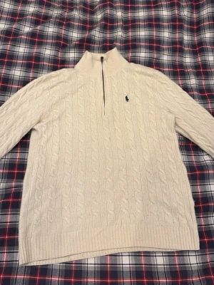  Polo Beige Cashmire Tröja - Säljer en beige kabelstickad tröja från Polo Ralph Lauren med half zip och hög krage. Tröjan har lång ärm, ribbade muddar och den klassiska broderade loggan på bröstet. Perfekt för kyliga dagar, köpt för 2300kr ish för 2 år sedan, här används kanske 10 gånger, men inte på ett tag, därav varför jag säljer den! 😁👍🏻🙏