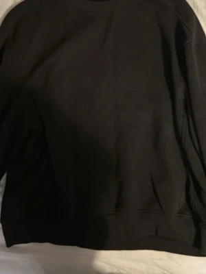 Svart sweatshirt från 157, storlek M - En klassisk svart sweatshirt från 157 i storlek M. Tröjan har rund halsringning och är tillverkad i mjukt material med borstad insida för extra komfort. Perfekt basplagg till garderoben.