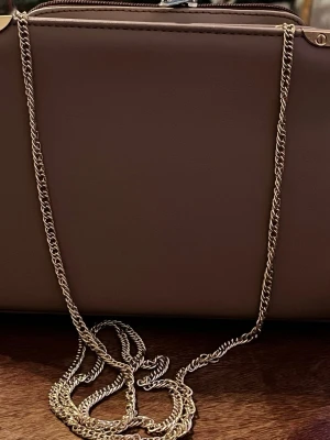 Dorothy Perkins  axelväska med guldkedja - Snygg brunrosa axelväska i slät skinnimitation med guldfärgad kedja som axelband. Väskan har flera fack inuti, inklusive ett med dragkedja, perfekt för att hålla ordning på smågrejer. Enkel och stilren design som passar till det mesta.