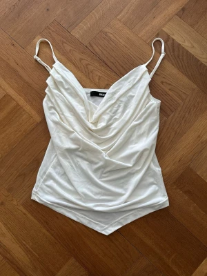 Vit linnetopp  - Säljer en vit linnetopp från Bik Bok. Toppen har en spetsig nederkant och är tillverkad i ett mjukt, glansigt material som känns lyxigt. Använd en gång.