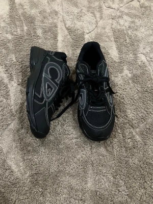 Svarta Stoe Island sneakers - Säljer ett par svarta sneakers från Stor Island med vita kontrastsömmar och logga broderad på hälen. Skorna har snörning, rund tå och en chunky sula. Materialmix av mesh och syntet ger en sportig vibe. Perfekta för dig som gillar streetwear och vill sticka ut.