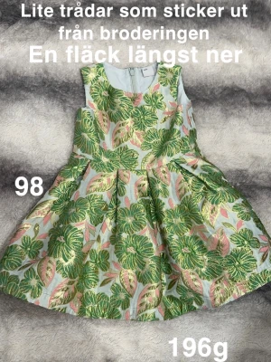 Blommig klänning med broderi - Supersöt klänning med broderade blommor i grönt och rosa på ljus botten. Ärmlös modell med rund hals och dragkedja bak. Kjolen är utställd och ger en riktigt fin siluett. Perfekt för sommarens alla tillfällen!🌸 Lite trådar som sticker ut från broderingen. En fläck längst ner. Storlek 98