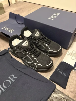 Svarta Dior B30 sneakers - Säljer ett par svarta Dior B30 sneakers med vita detaljer och reflekterande inslag. Skorna har mesh och syntetpaneler, rund tå och snörning. Tydlig Dior-logga på sidan och tungan. Riktigt snygga och trendiga sneakers för dig som vill sticka ut.