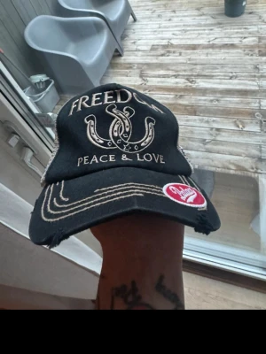 Palace truckerkeps svart/beige - Säljer en svart och beige truckerkeps från Palace med mesh på sidorna, broderade detaljer och texten 'FREEDOM PEACE & LOVE' framtill. Kepsen har coola patches, bland annat ett regnbågsfärgat peace-tecken och amerikainspirerad sköld på sidan.