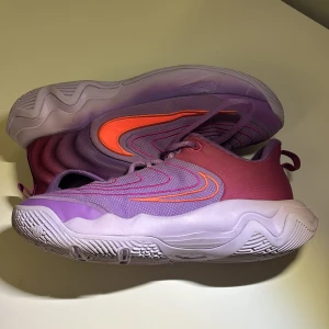 Basketskor (Giannis) -  Säljer ett par snygga Nike giannis basketskor i lila och orange med vågiga detaljer och en chunky, vit sula. Skorna har snörning och en sportig design med låg profil. Perfekt för dig som gillar färgstarka och unika sneakers.Använda ett par gånger, pris kan diskuteras