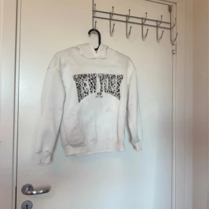 Vit hoodie med leopardmönster från SHEIN - Vit hoodie från SHEIN med coolt 'NEW YORK' tryck i leopardmönster på bröstet. Tröjan har huva, ribbade muddar och är långärmad. Perfekt för dig som gillar streetstyle och djurmönster. Materialet är mjukt och skönt, troligen bomull och polyester.