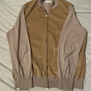 Gran sasso mockajacka i oanvänt skick - Snygg beige jacka från Gran Sasso med mockadetaljer på framstycket och mjuka stickade ärmar. Dragkedja framtill och ribbade muddar vid hals, ärmslut och nederkant. Perfekt för dig som gillar italiensk design och vill ha något som sticker ut. Helt oanvänd, storlek 54(XL) men passar L utmärkt. Ett plagg som verkligen sticker ut i mängden. Vid intresse kan fler bilder skickas och mått! Rekommenderar starkt 