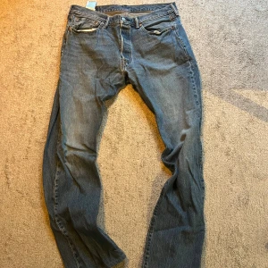 Levi's 501 blå jeans W34 L34 - Klassiska Levi's 501 jeans i blå denim med raka ben och fem fickor. Byxorna har knappgylf och den ikoniska läderpatchen bak i midjan. Perfekt passform och tidlös stil som funkar till allt. Storlek W34 L34. 