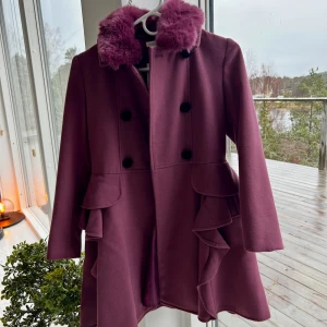 Lila kappa med volanger och päls! 💜💜 - Säljer en lila kappa med fluffig päls på kragen och snygga volangdetaljer längs sidorna. Dubbelknäppt framtill med svarta knappar och långärmad design. Perfekt för dig som vill sticka ut med en unik och trendig look. ❣️❣️ skriv gärna vid funderingar och intresse! 🌟💫