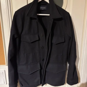 A Day's March Overshirt - Mörkblå overshirt-fieldjacka från A Day's March med klassisk krage och fyra stora fickor framtill. Jackan har knäppning med svarta knappar. Perfekt för lager-på-lager och stilren look.