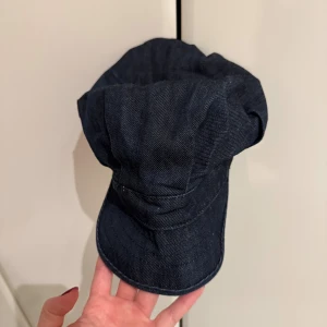 Denimkeps från Peak Performance - Snygg och unik mörkblå keps i denim från Peak Performance. Kepsen har en mjuk, lite puffig form med böjd skärm och elastisk baksida för skön passform.