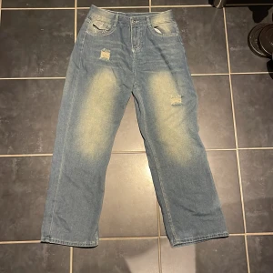 True Religion ljusblå washed jeans - Säljer ett par ljusblå jeans från True Religion med slitna detaljer framtill och ikoniska broderade bakfickor. Jeansen har klassisk femficksdesign, kontrastsömmar och en patch med Buddha på linningen. Perfekt för dig som gillar streetwear och vill sticka ut.