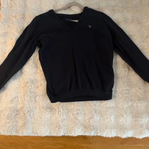Mörkblå v-ringad tröja från Gant - Snygg mörkblå v-ringad tröja från Gant med diskret logga broderad på bröstet. Tröjan har långa ärmar och ribbad kant vid midja och ärmslut. Perfekt för dig som gillar klassisk och stilren design. Storlek L men passar bra som oversize på s/m dam.