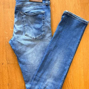 Jack & Jones Jeans - Säljer ett par klassiska blå jeans från Jack & Jones med snyggt slitna detaljer och femficksmodell. Jeansen har normal passform och raka ben, tillverkade i mjukt bomullsjeans-tyg. Perfekta för en avslappnad och stilren look.