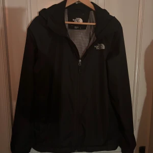 The North Face vindjacka - Svart vindjacka från The North Face med huva och dragkedja framtill. Jackan har meshfoder på insidan och logga på både bröstet och ryggen. Perfekt för blåsiga dagar och har en clean, sportig look som funkar till streetwear.🔥