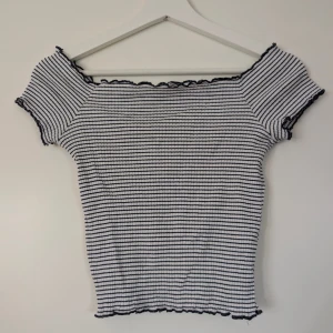 Randig ribbad topp från Zara Trafaluc - Säljer en vit och svart ribbad topp från Zara Trafaluc. Toppen har smala svarta ränder, korta ärmar och offshoulder-modell med vågig kant vid halsringning och nederkant. Perfekt för sommarens alla tillfällen!