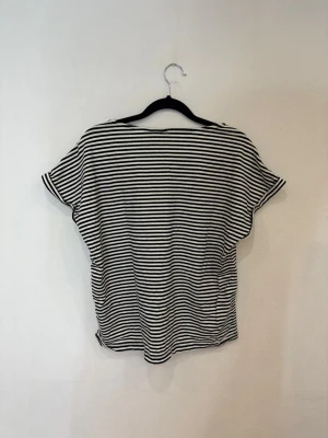 Svartvit randig topp med kort ärm - Säljer en svartvit randig topp med korta ärmar och rundad hals. Toppen har ett loose fit och är tillverkad i mjuk bomull, perfekt för en chill och stilren look. Ränderna är smala och går horisontellt över hela plagget.