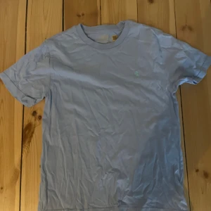 Ljusblå t-shirt från Polo Ralph Lauren - Snygg ljusblå t-shirt från Polo Ralph Lauren med klassisk passform och diskret broderad logga på bröstet. Tillverkad i mjuk bomull som känns skön mot huden. Perfekt för en avslappnad och stilren look.