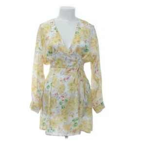 Blommig omlottklänning med bälte - Söt kort omlottklänning med blommigt mönster i ljusa toner av gul, grön och rosa på vit botten💖