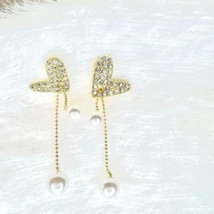 Glittriga hjärtformade örhängen med pärlor - Snygga örhängen med glittriga hjärtan i guld och hängande kedjor med vita pärlor. Örhängena är ca 4,5 cm långa och har en elegant design som verkligen sticker ut. Perfekta för dig som gillar att addera lite extra glamour till din look.