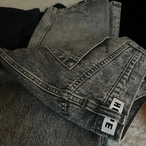 Gråa wide jeans från HOPE - Säljer ett par gråa stentvättade jeans från HOPE med raka, vida ben och klassisk femficksdesign. Jeansen har hög midja och HOPE-logga på hällan bak. Perfekta för dig som gillar en avslappnad och trendig look.