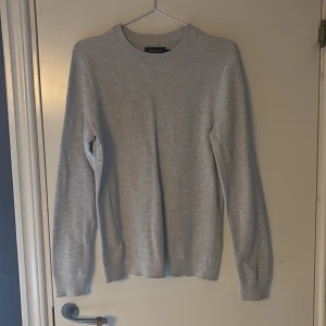 Ljusgrå stickad tröja från Riley - Säljer en stilren ljusgrå stickad tröja från Riley i storlek S. Tröjan har rund hals, diskret ribbade muddar och långärmad passform. Perfekt för dig som gillar enkel och clean stil. Materialet är mjukt och skönt mot huden.