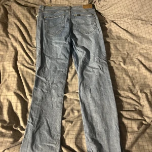 Ljusblå Lee jeans straight fit - Säljer ett par klassiska ljusblå jeans från Lee med rak passform. Jeansen har fem fickor, bälteshällor och Lee-logga på bakfickan samt läderpatch i midjan. Materialet är slitstarkt denim och modellen har dragkedja och knapp framtill.