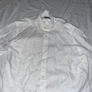 Oscar Jacobson Skjorta - Klassisk vit skjorta i linne med knäppning framtill och krage. Perfekt för en clean och fräsch look, passar till både jeans och shorts. Luftigt material som känns svalt och skönt.