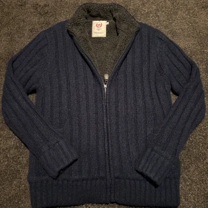 Fodrad Cardigan - Mysig mörkblå stickad teddy Cardigan från Atlantic Bay med fluffigt teddyfoder på insidan. Jackan har ribbade muddar, långärmad design och dragkedja framtill. Perfekt för kalla dagar när du vill ha både stil och värme.