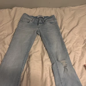 Ljusblå jeans G Rise - Snygga ljusblå jeans från Gena Jeans G Rise med klassisk femficksdesign och slitning på ena benet för en cool look. Jeansen är utsvängda och kontrastsömmar på bakfickorna.❤️❤️ storlek S