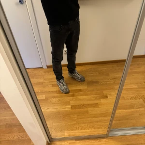 Nudie Jeans Grim Tim 30/30 - Säljer ett par svarta Nudie Jeans Grim Tim i modellen Dark Cove. De har en slim passform med raka ben och klassisk femficksdesign. Materialet är 99% bomull och 1% elastan för lite stretch. Snygga och stilrena jeans som funkar till det mesta. Storlek 30/30. Jeansen är i bra skick och har inga defekter.