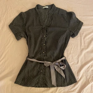 Prickig blus - Prickig figursydd brun-grå blus med ett knytbart band som även går att ta bort. Strl M