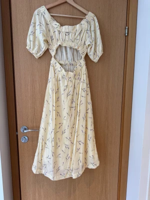 Blommig ljusgul klänning från H&M - Supersöt ljusgul klänning från H&M i 100% bomull med lila blommönster. Klänningen har puffärmar som kan bäras både offshoulder och vanligt, smock upptill och i midjan samt en mjuk, flowy siluett som slutar strax under knät. Perfekt för sommarens alla tillfällen! Mönstrad ljusgul (butter yellow) blommig midiklänning med lila lavendel blommor, midilängd, underkjol, öppning i ryggen, puffärm eller off-sholder. Storlek XS-S.