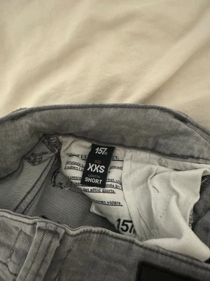 Grå jeans med broderade bakfickor XXS - Säljer ett par grå jeans från 157 i storlek XXS Short. De har låg midja, raka ben och snygga broderade detaljer på bakfickorna. Jeansen har dubbla knappar fram och är tillverkade i mjukt denimtyg som sitter skönt.