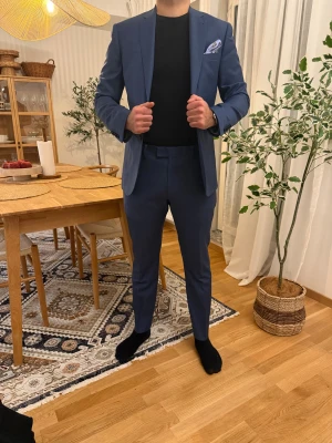 Blå kostym från Riley - Säljer en stilren blå kostym från Riley. Kavajen har klassisk passform med två knappar, fickor och matchande byxor. Fodret är svart med beige detaljer. Perfekt för dig som vill ha en snygg och modern look. Kavaj, storlek 50. Byxor, storlek 52. Dvs, kavaj känns som M och byxorna 33-34/32. 