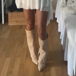 Beiga mockastövlar med spetsig tå - Säljer ett par snygga beiga stövlar i mocka med spetsig tå och klack. Stövlarna har en slouchy passform som ger en cool och avslappnad vibe. Perfekta att styla med kjol eller klänning för en trendig look.