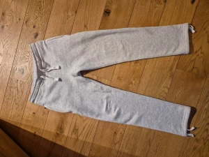 Grå mjukisbyxor från Russermerch, storlek xs - Snygga ljusgrå mjukisbyxor från russermerch i storlek xs. Byxorna har snörning i midjan, ribbad linning och snöten vid bensluten. Mjukt material, med fickor fram och en bakficka. Perfekta för chill eller träning. UNISEX 