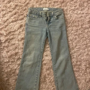 Ljusblå bootcut jeans från Perfect Jeans - Säljer ett par ljusblå jeans från Perfect Jeans i klassisk bootcut-modell. Jeansen har låg midja, fem fickor och snygga detaljer på bakfickorna med knappar. Tillverkade i jeansmaterial med dragkedja och knapp framtill. 