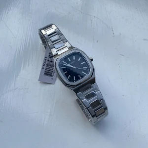 Klcoka - BUTIKSPRIS 3049kr. Stilren klocka från Faucon med svart urtavla och datumvisning. Boetten är åttakantig och armbandet är i silverfärgad metall med snygg länkdesign. Klockan har minimalistiska index och klassisk krona på sidan. Perfekt accessoar för en clean look. PRISET KAN DISKUTERAS.