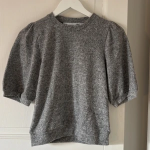 Grå puffärm tröja från 157 - Mysig grå tröja från 157 med puffade ärmar och rund hals. Materialet är mjukt och känns som bomull, perfekt för dig som gillar enkel men snygg stil. Passformen är normal och ärmarna är lite kortare än vanligt, vilket ger en cool look.