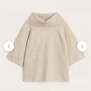 Beige stickad polotröja med vida ärmar - Beige stickad polotröja med bred krage och trekvartsärmar. Tröjan har en loose passform och är tillverkad i ett mjukt material som känns skönt mot huden. Perfekt för lager-på-lager och chill stil.