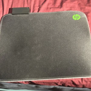 HP Pavilion Gaming Mouse Pad 400 - HP Pavilion Gaming Mouse Pad 400 med USB-port, perfekt för gaming och arbete. Slitstark yta och sydda kanter. Några mindre tecken på användning, men i gott skick. Kompatibel med de flesta datormöss och har en snygg HP-logga i hörnet.
