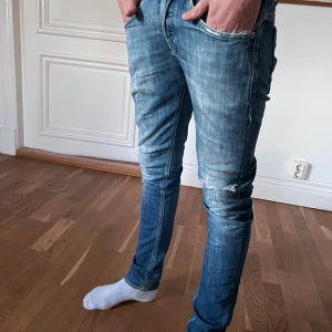 Dondup George  - Säljer ett par blå dondup jeans med snygga slitningar vid knäna och bakfickor med dragkedjedetaljer. Perfekta för dig som gillar en modern och avslappnad stil.
