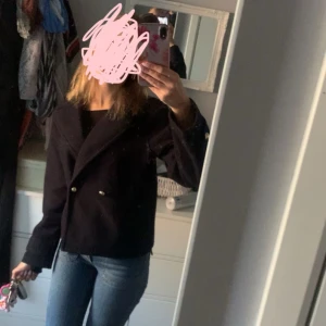 Mörkblå kappa från Gina Tricot - Snygg mörkblå kappa från Gina Tricot med bred krage och dubbla knappar framtill. Jackan har två fickor och dekorativa knappar vid ärmsluten. Perfekt för dig som gillar klassisk stil med en modern twist.💕