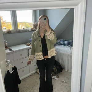 Grön kort jacka med spets från Zara - Säljer en ljusgrön kort jacka från Zara Woman med snygga krämvita spets- och volangdetaljer vid ärmslut och nederkant. Jackan har knappar framtill och är långärmad. Perfekt för dig som vill sticka ut med en unik och trendig look.