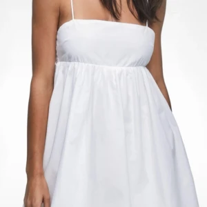 Vit kort sommarklänning med tunna band - Superfin vit kort klänning med tunna axelband och rakt skuren överdel. Klänningen har en luftig, utställd kjol och är perfekt för varma dagar. Enkel och stilren design som känns fräsch och trendig. Materialet är lätt och känns skönt mot huden.
