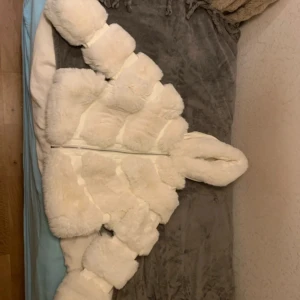 Vit pälsjacka med huva från Boohoo - Supermjuk och fluffig vit pälsjacka från Boohoo med stor huva och dragkedja framtill. Jackan har en oversized look och är fodrad på insidan för extra värme. Perfekt för kalla dagar när du vill sticka ut och hålla dig varm.