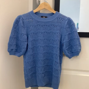 Blå stickad topp med puffärm C&A XS - Supersöt ljusblå stickad topp från C&A i storlek XS. Tröjan har korta puffärmar, rund halsringning och ett genomgående hålmönster som ger en luftig känsla. Perfekt för vår och sommar när du vill ha något både gulligt och bekvämt. Aldrig använd