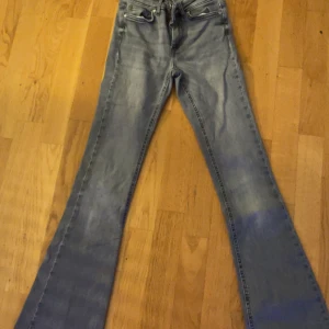 Grå bootcut jeans från ONLY - Snygga grå jeans från ONLY med bootcut passform och klassisk femficksdesign. Jeansen har mid/low midja och är tillverkade i mjukt denim-material med dragkedja och knapp framtill. Perfekt för dig som gillar retrovibbar och vill ha ett par jeans som sticker ut.